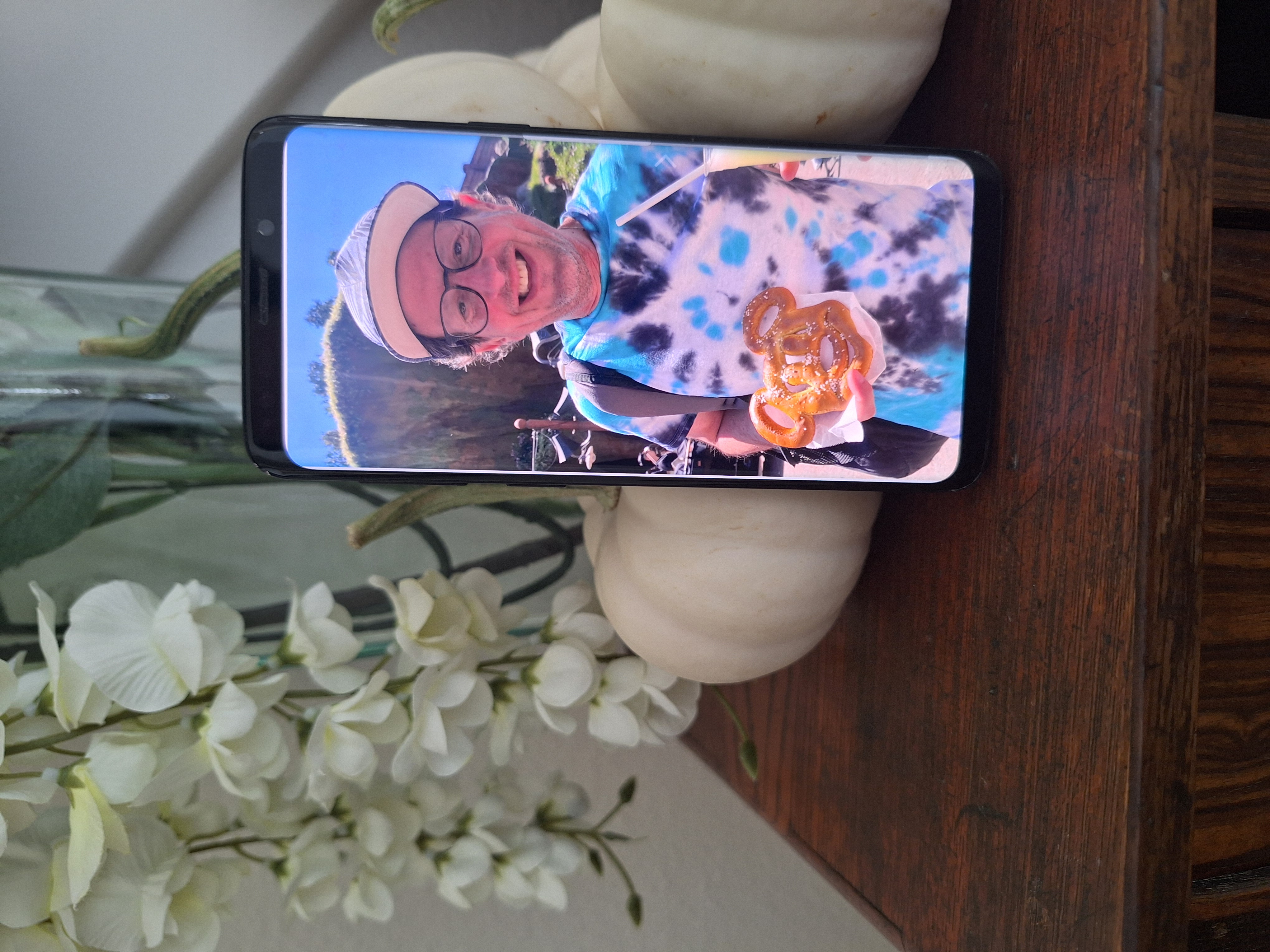 A phone displaying a vacation photo beside a vase at home.