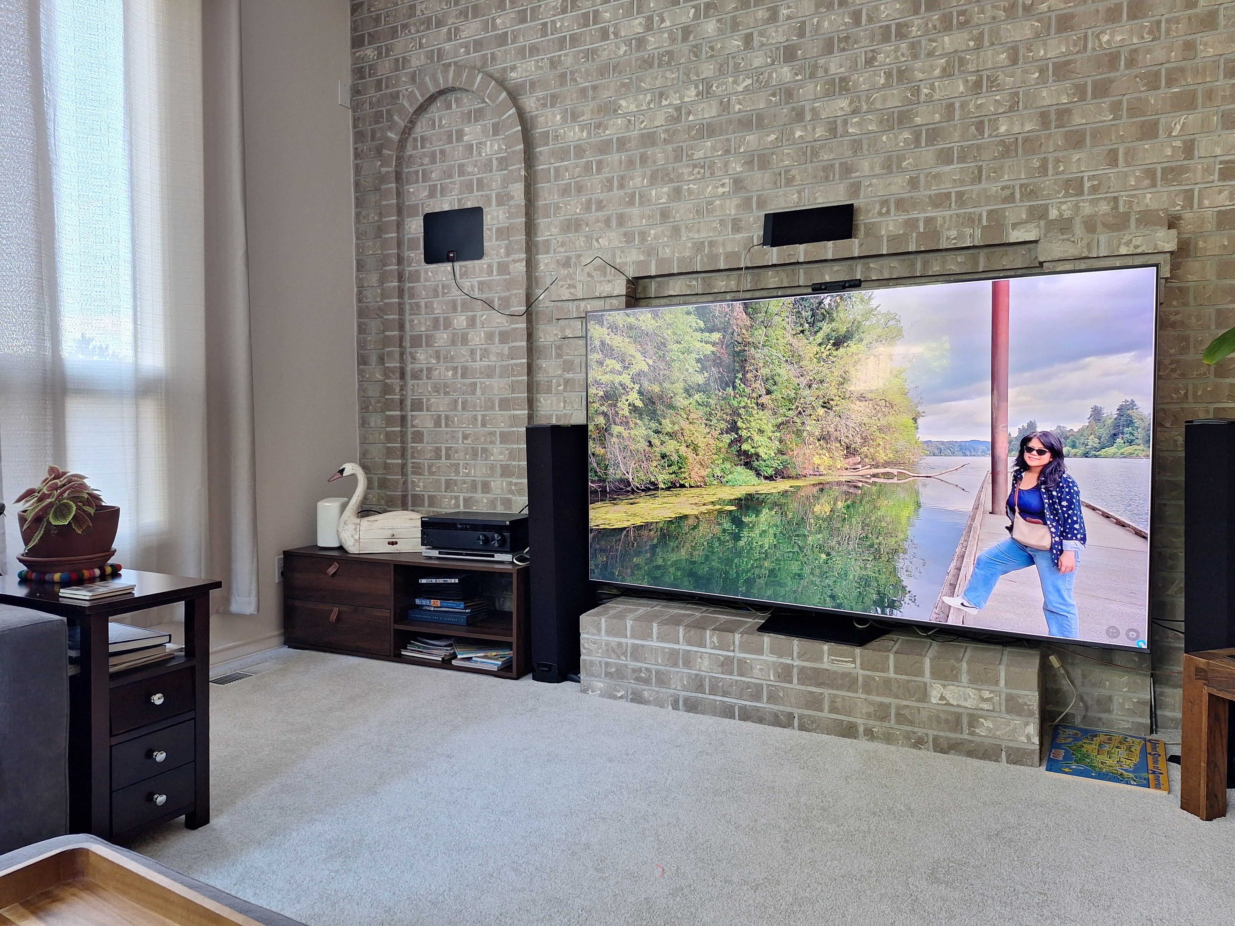 A family-room TV beside the brick fireplace displays one large photo of a woman by a lake.