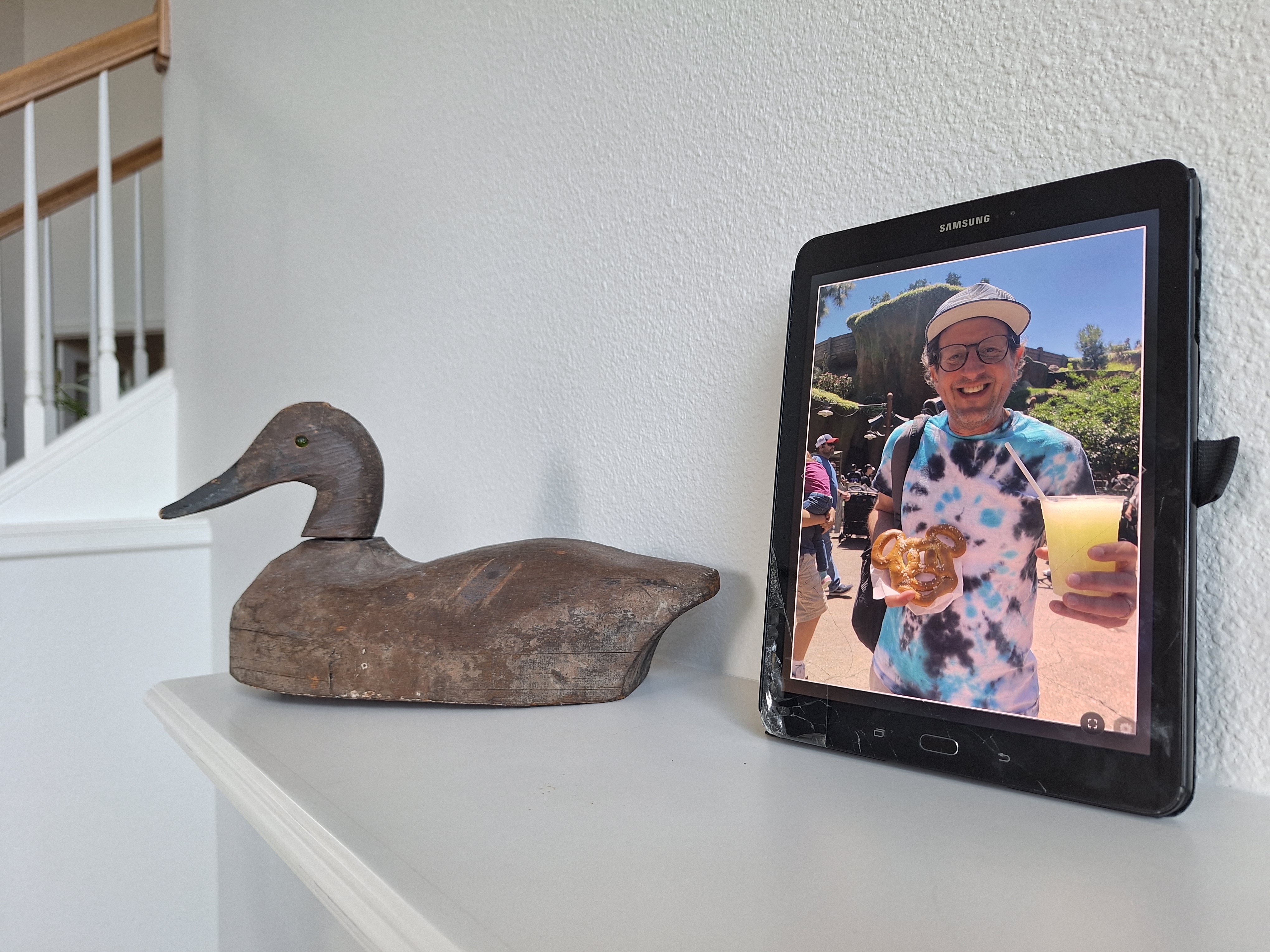A tablet running AnyFrame displays a vacation photo beside a wooden duck at home.